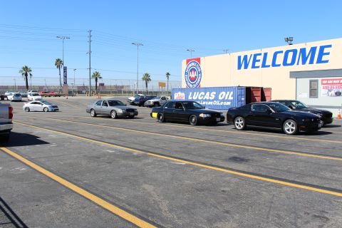 2003 Ford Crown Victoria - Several dark sedans parked across yellow-striped lot in front of a tan building marked WELCOME, with a Lucas Oil shipping container behind…