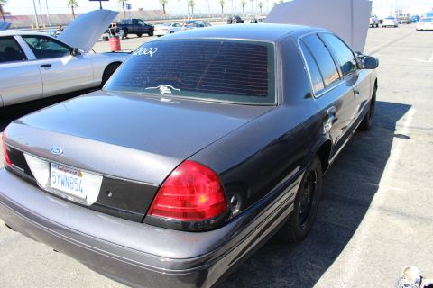 2003 Ford Crown Victoria - Rear three-quarter view of a dark gray Ford Crown Victoria sedan with a California plate, parked among other cars in a lot.