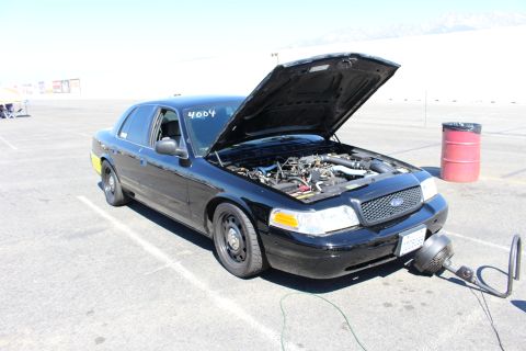 2003 Ford Crown Victoria - black Ford Crown Victoria with its hood raised and 4004 marked on the windshield, staged on open pavement with a cooling fan in front.