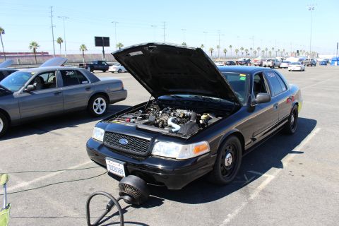 2003 Ford Crown Victoria - black Ford Crown Victoria with its hood up and a portable cooling fan in front of the grille, parked among other sedans at a track lot.