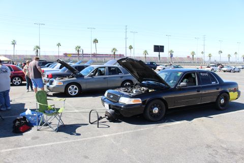 2003 Ford Crown Victoria - row of Ford Crown Victoria sedans with hoods raised at a track meet, with a black 4004 car in front beside a camping chair and cooler.