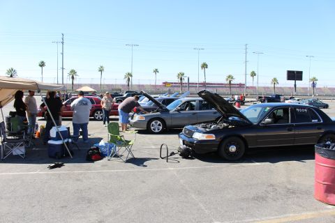2003 Ford Crown Victoria - People gather among Ford Crown Victoria sedans with raised hoods at a track lot, with canopies, chairs and coolers set up alongside.