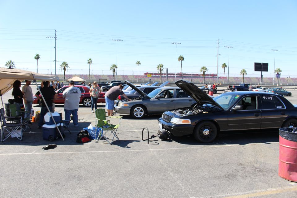 People and Crown Victoria sedans with hoods up under canopy at track lot