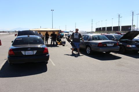 2003 Ford Crown Victoria - group of people stand among Ford Crown Victoria sedans at a track lot, with a black 4004 car at left and a freight train in the distance.