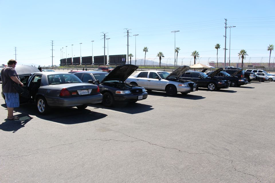 Long row of Crown Victoria sedans with hoods up at a track lot