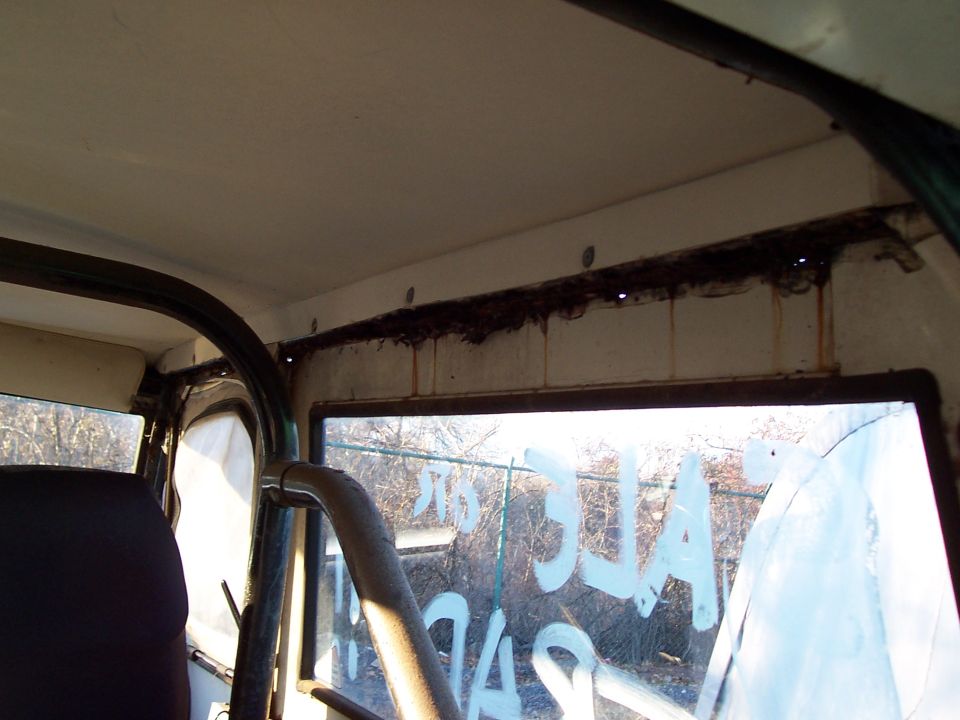 Interior view of a vehicle showing a roll cage, dark seat, and writing on the window