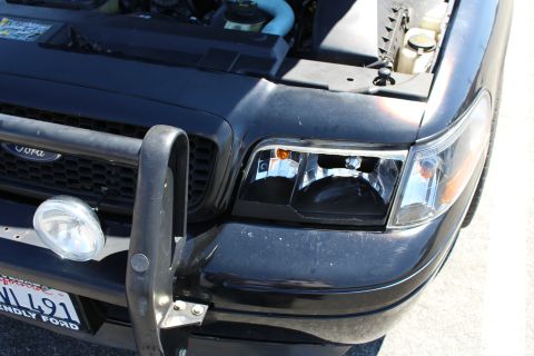 2003 Ford Crown Victoria - Front corner of a black Ford with a push bar, auxiliary spotlight, clear headlight and Ford oval grille, with a partial California plate.