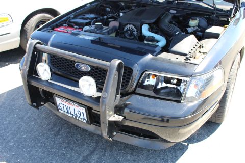2003 Ford Crown Victoria - Front of a black Ford Crown Victoria with hood raised, a push bar with dual spotlights, Ford oval grille and California plate 6TVL491.