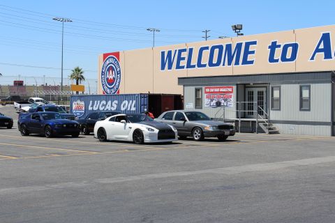 2003 Ford Crown Victoria - white Nissan GT-R, a blue Mustang and a gray sedan park beside a Lucas Oil container under an 'AUTO CLUB' welcome sign.