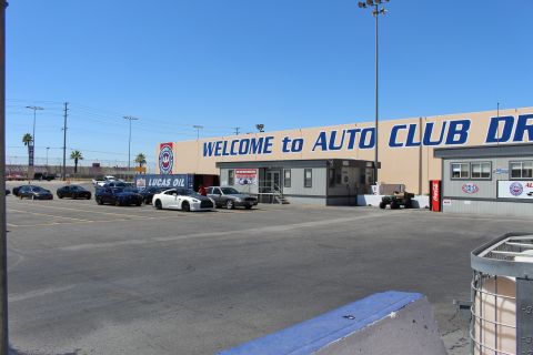 2003 Ford Crown Victoria - tan track-tower building reading 'WELCOME to AUTO CLUB DR' sits over a paved lot with parked cars and a Lucas Oil banner.
