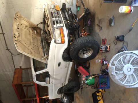 1994 Ford Bronco - This lifted pickup truck is undergoing maintenance in a workshop, surrounded by various tools and equipment.