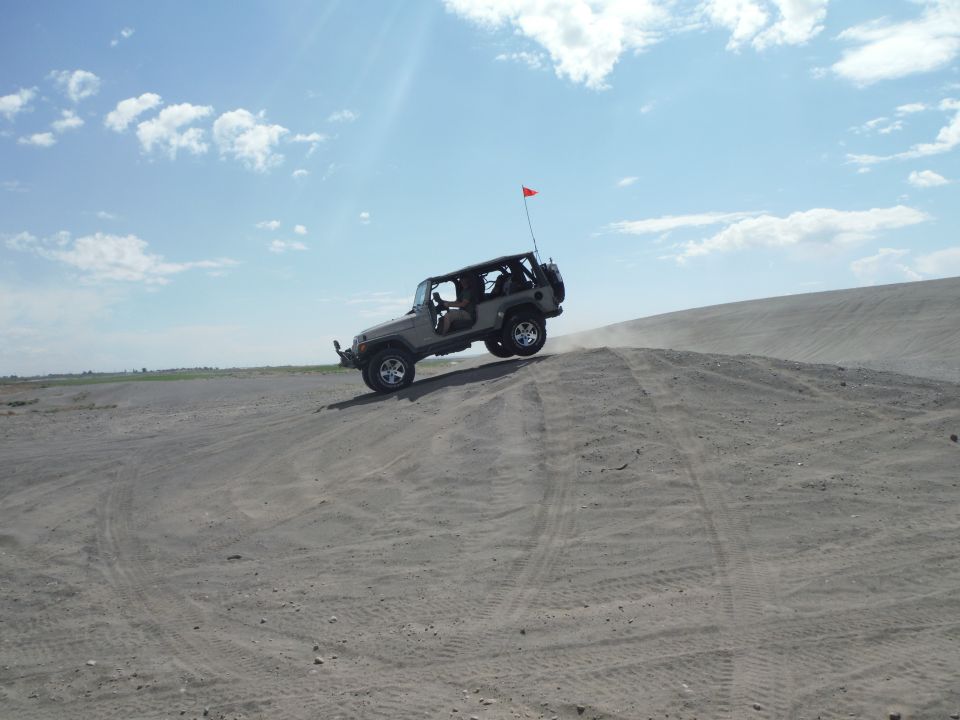 Silver 2005 Jeep Wrangler climbing a sand dune with a red flag on antenna