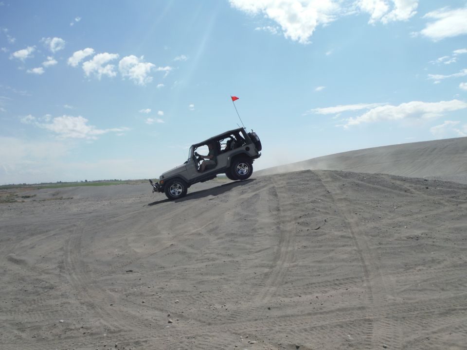 Jeep Wrangler driving up a sand dune with a red flag on antenna. It's a 2007 model