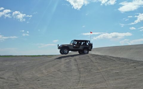 2005 Jeep Wrangler - A Jeep Wrangler takes flight over a sand dune under a partly cloudy sky.