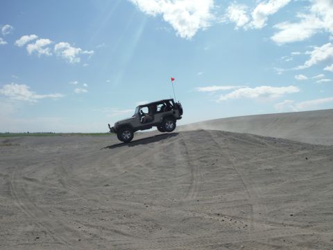 2005 Jeep Wrangler - Jeep Wrangler cresting a sand dune under a partly cloudy sky.