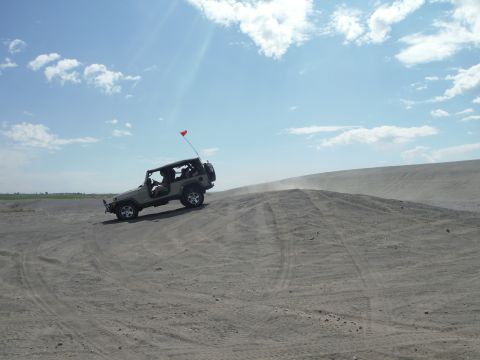 2005 Jeep Wrangler - A Jeep Wrangler navigates a sand dune under a partly cloudy sky.