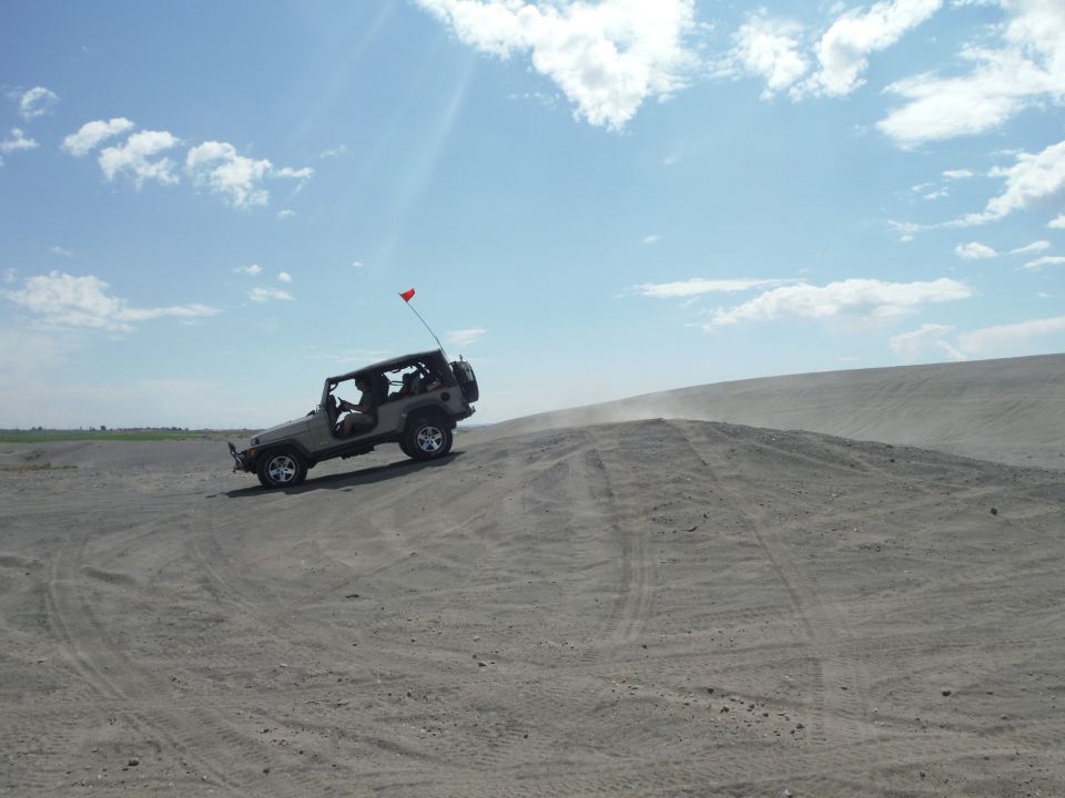 Silver Jeep Wrangler driving up a sand dune, red flag on antenna