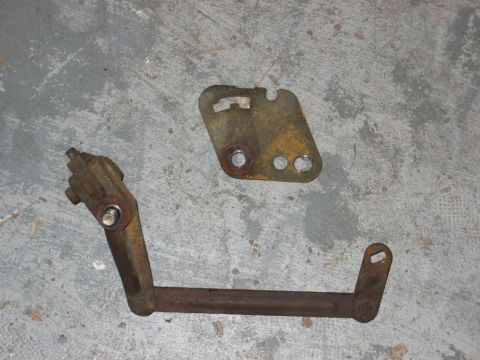 1993 Ford F-150 - Two rusted metal automotive parts are shown on a concrete surface, with one part being a bracket and the other a bent rod.