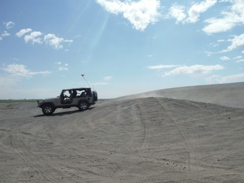 2005 Jeep Wrangler - A tan 2005 Jeep Wrangler navigates a sandy terrain on a bright, partly cloudy day.