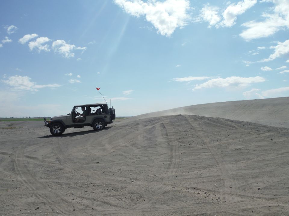 Tan 2005 Jeep Wrangler driving on a sand dune under a blue sky