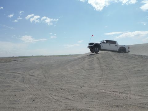 2005 Jeep Wrangler - Pickup truck driving on a sand dune with a red flag attached.
