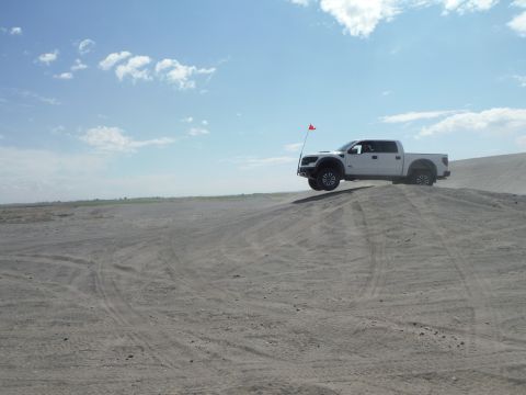 2005 Jeep Wrangler - A white pickup truck is captured mid-air as it jumps over a sand dune under a partly cloudy sky.