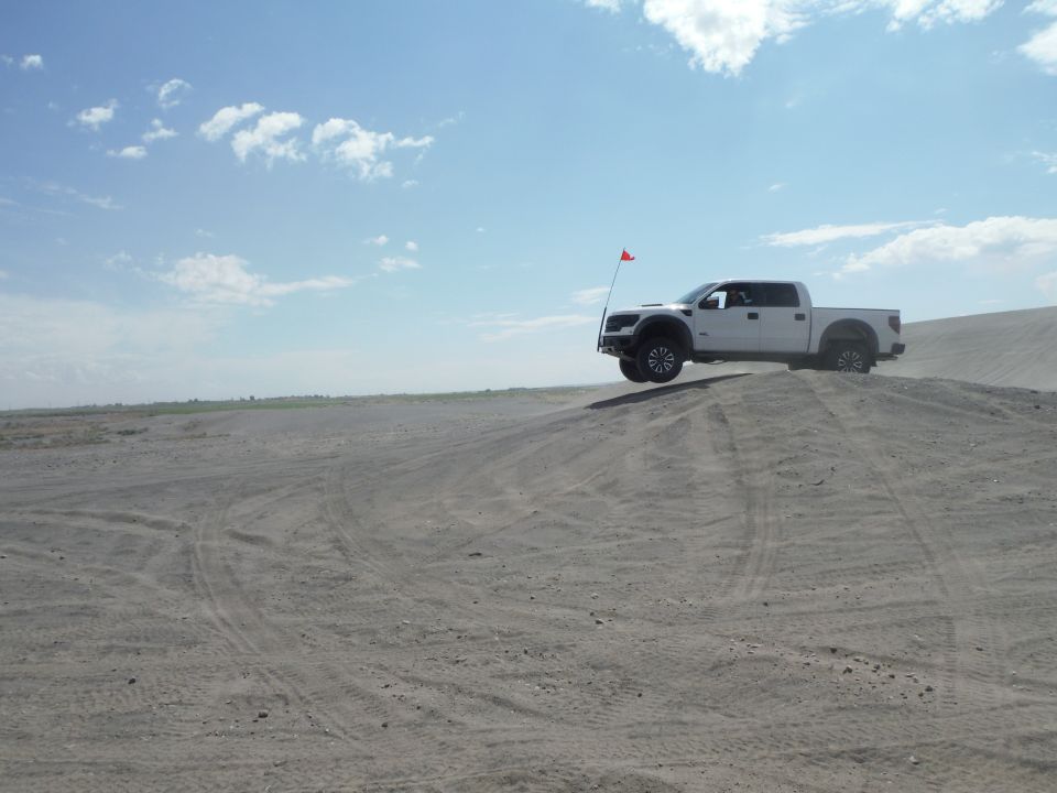 White pickup truck airborne over a sand dune with a red flag on an antenna
