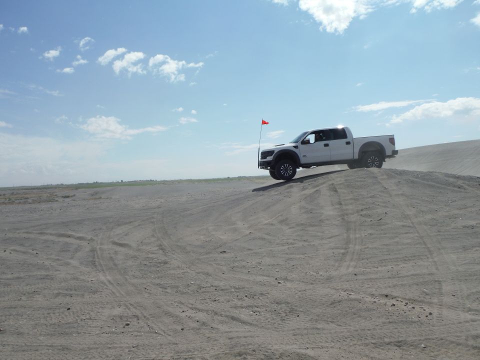 White pickup truck with a red flag on a sand dune under a cloudy sky