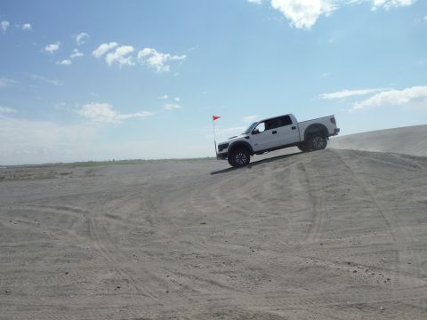 2005 Jeep Wrangler - A white pickup truck navigates a sandy incline under a partly cloudy sky. The vehicle appears to be a 2010 model.