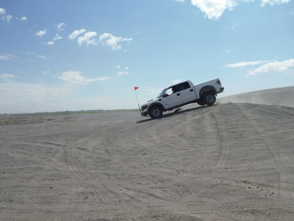 White Ford F-150 Raptor driving up a sand dune with a red flag attached to antenna