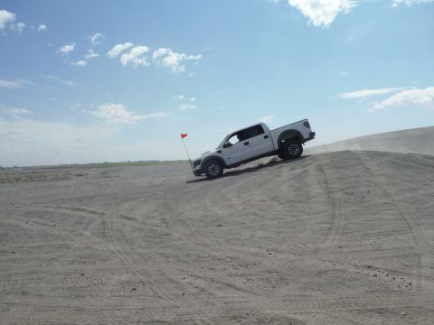 2005 Jeep Wrangler - A white pickup truck navigates a sandy incline under a partly cloudy sky.