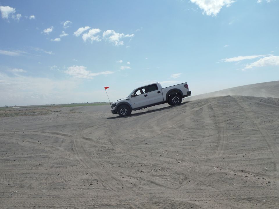 White pickup truck with red flag driving up a sand dune