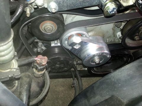 2003 Ford Crown Victoria - serpentine belt routes over a polished aluminum belt tensioner and grooved idler pulleys deep in an engine bay.