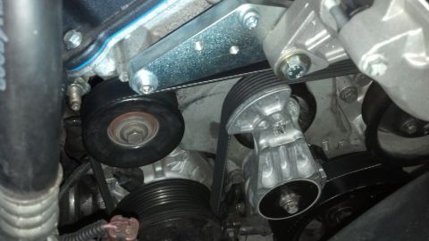 2003 Ford Crown Victoria - polished aluminum belt tensioner and idler pulleys guide a serpentine belt within a tight engine bay.