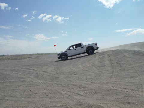 2005 Jeep Wrangler - Pickup truck navigates a sandy incline on a clear day.