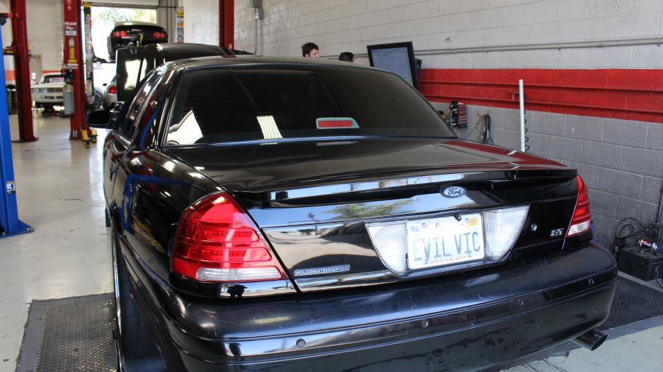 Rear three-quarter of black Ford sedan with EVIL VIC plate inside garage