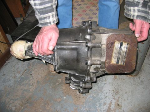 1993 Ford F-150 - A transmission part is held by two people, with a label visible on a rusty plate.