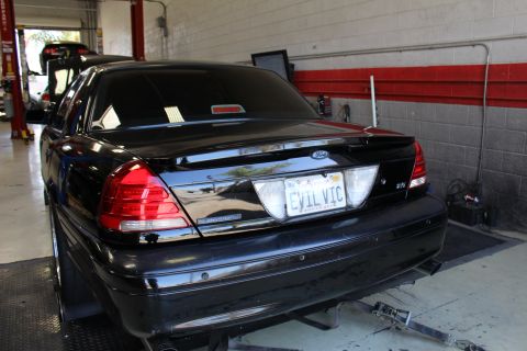 2003 Ford Crown Victoria - Black Ford sedan parked in a garage bay, rear three-quarter view, with a California EVIL VIC vanity plate.