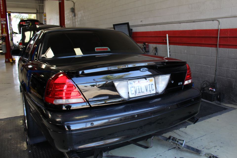 Rear three-quarter of black Ford sedan with EVIL VIC plate in shop bay