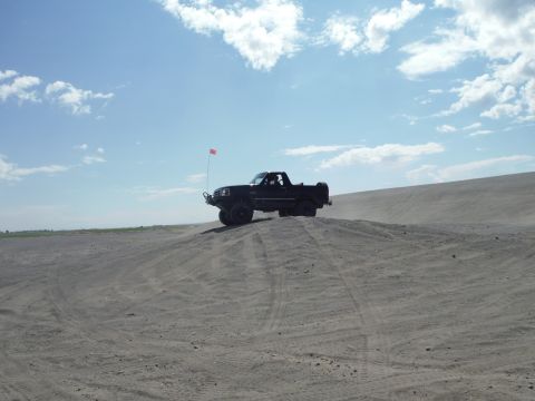 2005 Jeep Wrangler - A black pickup truck navigates a sandy incline, a small red flag fluttering from its antenna.