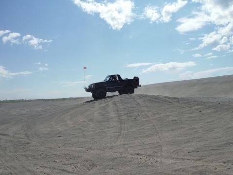 2005 Jeep Wrangler - A black pickup truck navigates a sandy terrain under a partly cloudy sky.