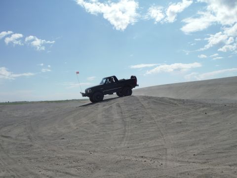 2005 Jeep Wrangler - A black pickup truck navigates a sandy terrain under a partly cloudy sky.