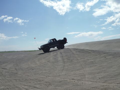 2005 Jeep Wrangler - A black pickup truck navigates a sandy incline under a bright blue sky with scattered clouds.