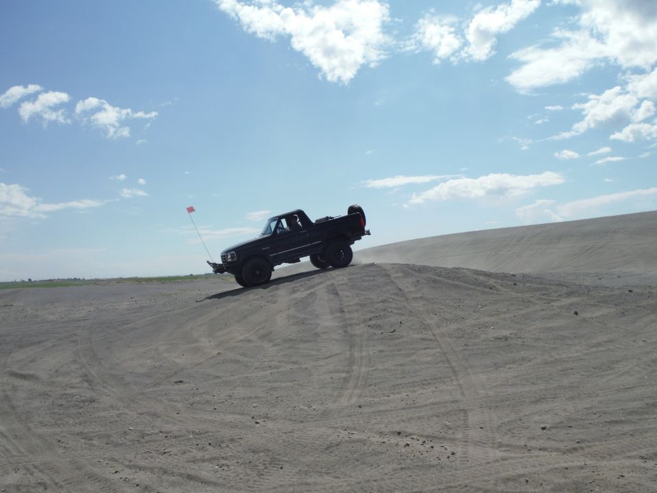Black pickup truck driving on a sand dune, 3q-front view