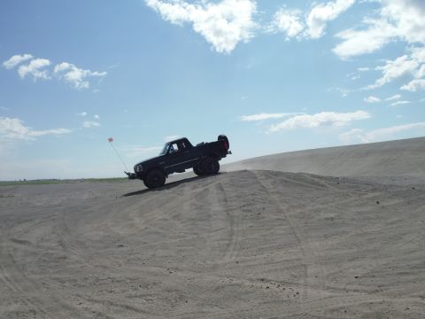 2005 Jeep Wrangler - A black pickup truck navigates a sandy incline under a partly cloudy sky.