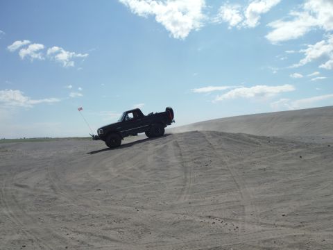 2005 Jeep Wrangler - A black pickup truck navigates a sandy incline under a partly cloudy sky.