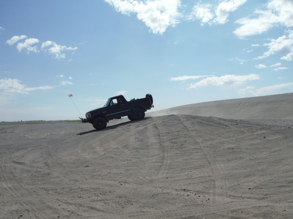 Black pickup truck on sand dune with flag