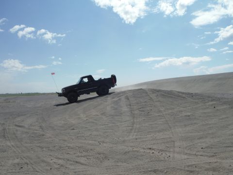 2005 Jeep Wrangler - Pickup truck navigates a sandy incline under a partly cloudy sky.
