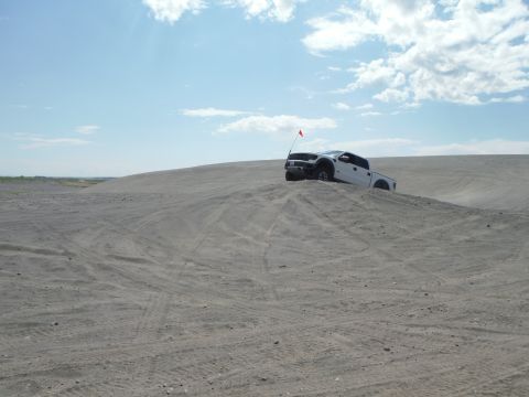 2005 Jeep Wrangler - A white pickup truck navigates a sandy terrain on a bright, partly cloudy day.