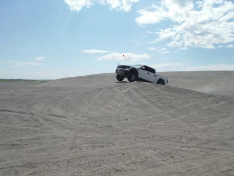 2005 Jeep Wrangler - A white pickup truck navigates a sandy incline under a partly cloudy sky.